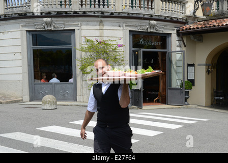 Serveur italien crossing road avec bac alimentaire Bellagio sur le lac de Côme Italie / service serveurs restaurant Italien Banque D'Images