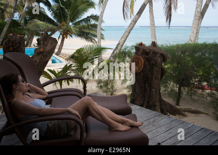 L'île de Rarotonga. L'île de Cook. Polynésie française. Océan Pacifique Sud. Client d'une femme se détendre sur une chaise longue au bord de la mer dans l'luxurio Banque D'Images