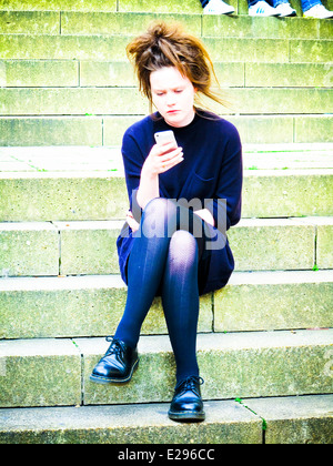 Young girl looking at phone sitting on steps Banque D'Images