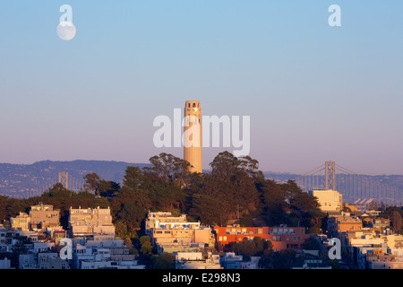 Vue de la Coit Tower et le Bay Bridge avec une pleine lune se levant au coucher du soleil à San Francisco, Californie. Banque D'Images