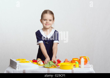 Petite fille de cinq ans jouant dans une aire de mistress plats à une table couverte d'un chiffon Banque D'Images