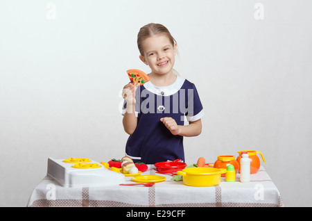 Petite fille de cinq ans jouant dans une aire de mistress plats à une table couverte d'un chiffon Banque D'Images