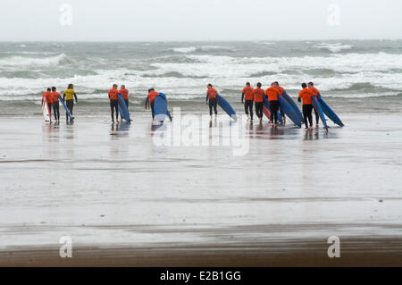 L'Irlande, le comté de Kerry, pouce, les surfeurs marche sur la plage, dans le mauvais temps Banque D'Images