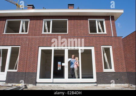 Jeune couple avec le plan directeur est à l'extérieur de la vue joyeusement de leur nouvelle maison. Banque D'Images