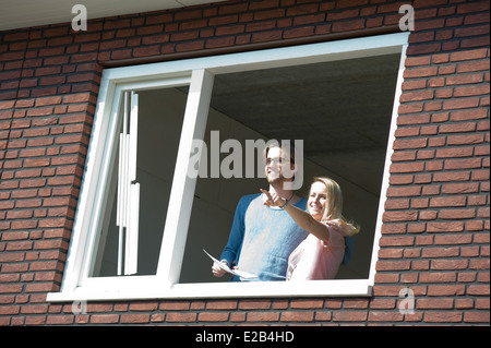 Jeune couple avec le plan directeur est à l'extérieur de la vue joyeusement de leur nouvelle maison. Banque D'Images