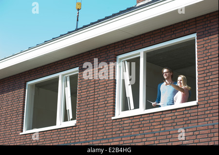 Jeune couple avec le plan directeur est à l'extérieur de la vue joyeusement de leur nouvelle maison. Banque D'Images