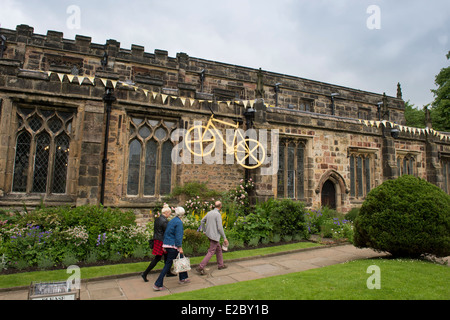 3 personnes passent devant l'église Holy Trinity, Skipton, décoré avec grand Yellow Bike & bunting flags célèbre Tour de France - le Yorkshire. Angleterre, Royaume-Uni. Banque D'Images