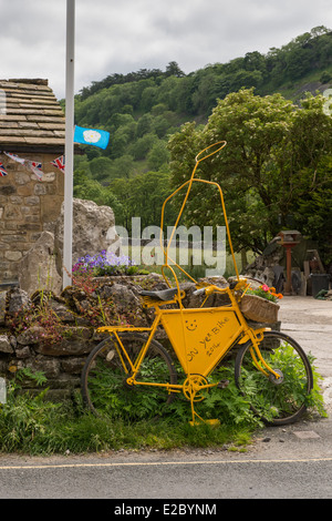 Vélo Jaune décoratifs & son 'rider', sont appuyés contre un mur de pierre en village Kettlewell promotion Tour de France - North Yorkshire, Angleterre, Royaume-Uni. Banque D'Images