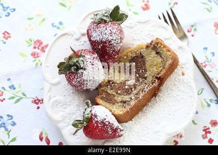 Tranche de gâteau avec des fraises fraîches saupoudrées de sucre en poudre sur un fond tissu floral vintage Banque D'Images