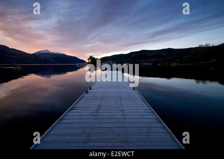 Le lever du soleil les couleurs sur un loch Lomond encore avec la jetée de inveruglus menant dans le loch Banque D'Images