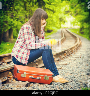 Sad girl avec valise rétro et bouquet de pissenlits assis sur les rails Banque D'Images