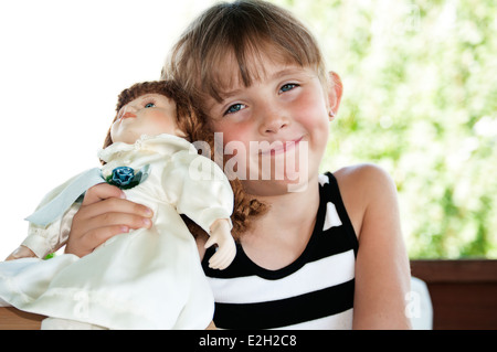 Cute little girl sourit de contentement qu'elle détient sa poupée fermer. Banque D'Images