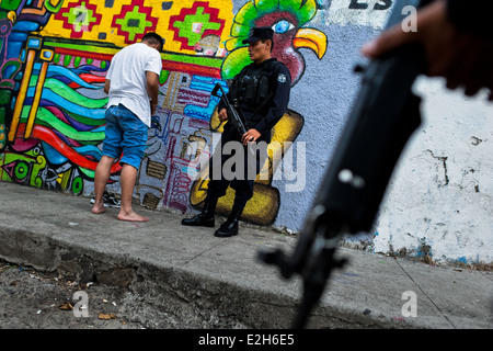 Un présumé membre d'un gang est contrôlé par un policier de l'unité spéciale d'urgence dans la rue à San Salvador, El Salvador. Banque D'Images