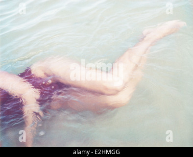 Femme couchée sur le côté dans une eau peu profonde, cropped view Banque D'Images