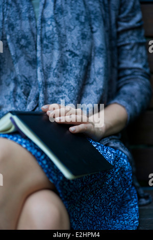 Femme assise avec livre ouvert reposant sur les genoux, cropped Banque D'Images