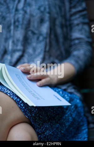 Femme assise avec livre ouvert reposant sur les genoux, cropped Banque D'Images