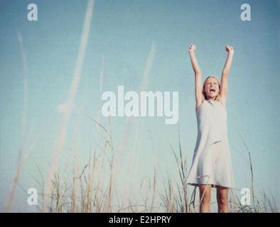 Young woman standing in field with arms raised, criant, low angle view Banque D'Images