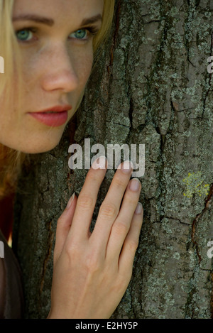 Young woman leaning against tree trunk avec expression rêveuse Banque D'Images