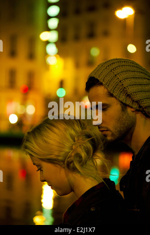 Jeune couple dans la nuit par la rivière illuminée par les lumières de la ville Banque D'Images