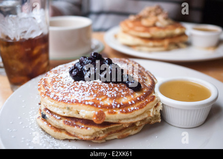 Pile de crêpes américaines moelleuses garnies de myrtilles et de sucre en poudre, servies avec du sirop d'érable dans un restaurant. Banque D'Images