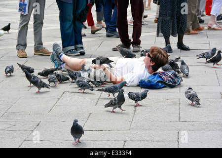 Femme portant sur dalles parmi les touristes à la place St Marc Venise nourrir les pigeons de ses mains Banque D'Images