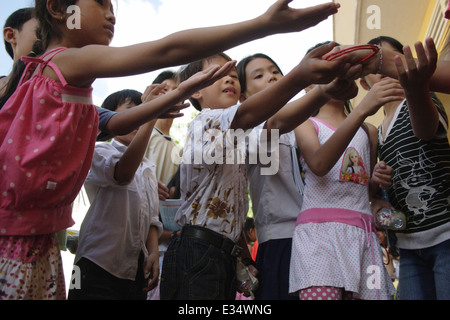 Les enfants sont en train d'atteindre avec leurs mains pour recevoir les jouets à une assemblée générale à l'École d'Angkor à Kampong Cham, au Cambodge. Banque D'Images