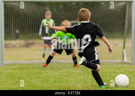 Gardien et peine kicker au milieu d'un coup de pied de pénalité lors d'un match de soccer pour les jeunes. L'accent est mis sur le kicker. Banque D'Images