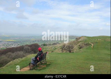 Femme Walker avec un chien Schnauzer miniature Assis sur un banc Surplombant Cheltenham et les Cotswolds, Gloucestershire, Angleterre, Royaume-Uni Banque D'Images