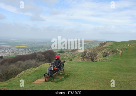 Femme Walker avec un chien Schnauzer miniature Assis sur un banc Surplombant Cheltenham et les Cotswolds, Gloucestershire, Angleterre, Royaume-Uni Banque D'Images