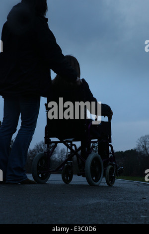 Femme de pousser une jeune fille assise dans un fauteuil roulant. Banque D'Images