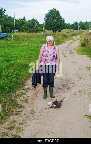 L'été 2013 vie rurale. La femme et le chat sur la route dans le village. Banque D'Images