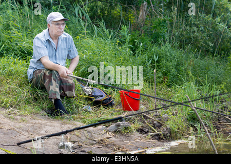 Hauts homme handicapé d'une amputation au-dessus du genou la pêche sur un lac avec une canne et moulinet contre un écrin de verdure Banque D'Images