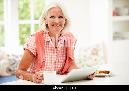 Middle aged Woman Using Digital Tablet pendant le petit-déjeuner Banque D'Images