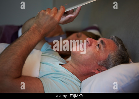 Couple d'âge moyen au lit avec Man Using Tablet Computer Banque D'Images