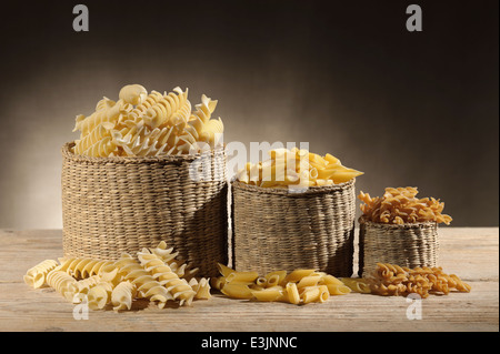 Des paniers de paille avec variété de pâtes alimentaires non cuites sur table en bois Banque D'Images