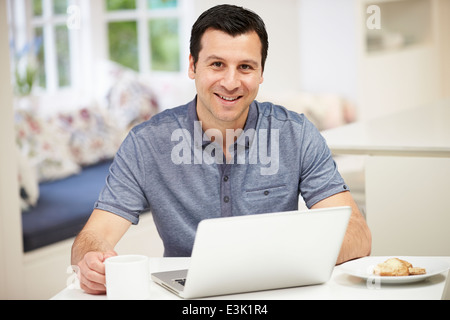 Hispanic Man Using Laptop In Cuisine à la maison Banque D'Images