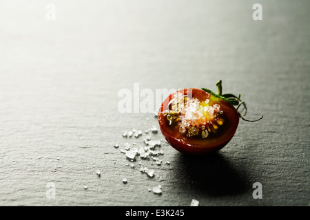 Tomates Raisins frais avec du sel pour une utilisation comme ingrédients de cuisson de moitié avec une tomate dans le premier plan avec copyspace Banque D'Images