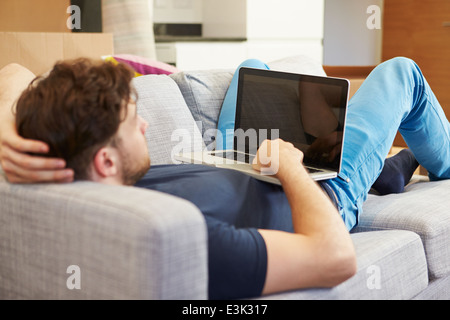 Man Relaxing On Sofa With Laptop In New Home Banque D'Images