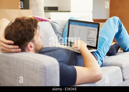 L'homme en utilisant les services bancaires en ligne Relaxing On Sofa Banque D'Images