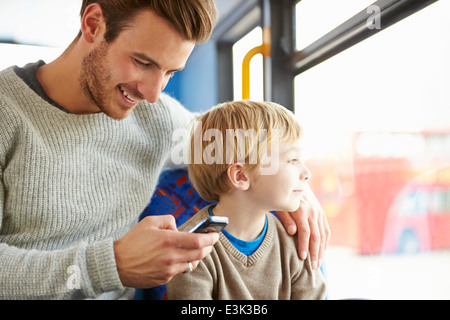 Père Using Mobile Phone On voyage en bus avec fils Banque D'Images