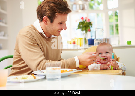 Père nourrir bébé assis dans une chaise haute à l'heure du repas Banque D'Images
