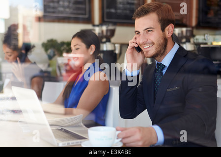 Businessman Using Mobile Phone and Laptop in Coffee Shop Banque D'Images