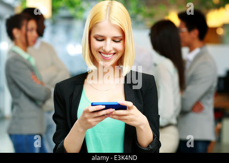 Happy businesswoman using smartphone devant des collègues Banque D'Images