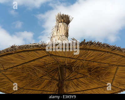 Détail d'un article de parapluie parasol de paille à la recherche jusqu'à la face inférieure contre un ciel bleu avec des nuages Banque D'Images