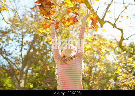 Jeune Fille de jeter les feuilles d'automne dans l'air Banque D'Images