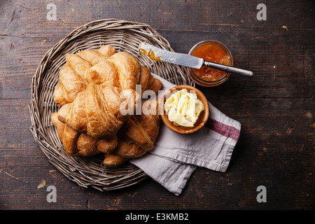 Les croissants avec du beurre et de la confiture dans le bac en osier foncé sur fond de bois Banque D'Images