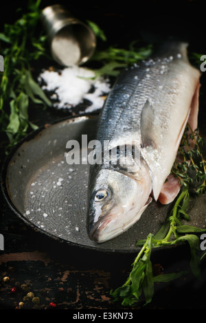 Loup de mer poisson cru servi avec des fines herbes et de sel de mer sur vintage casserole à table en bois noir Banque D'Images