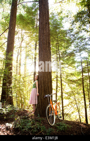 Woman leaning against tree in forest Banque D'Images