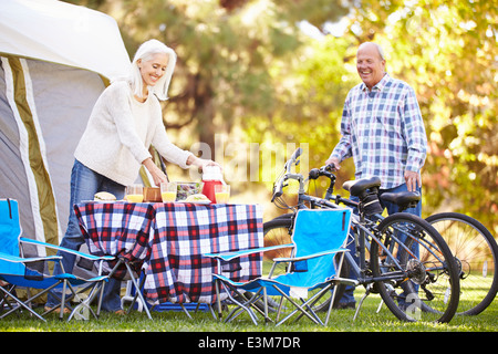 Senior Couple Riding Bikes On Camping Holiday In Countryside Banque D'Images