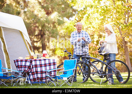 Senior Couple Riding Bikes On Camping Holiday In Countryside Banque D'Images